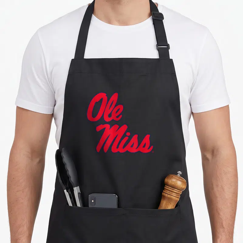 Ole mississippi girl apron - Red script Ole Miss text with blue outline on black fabric — shown on a black cotton canvas apron against a white background