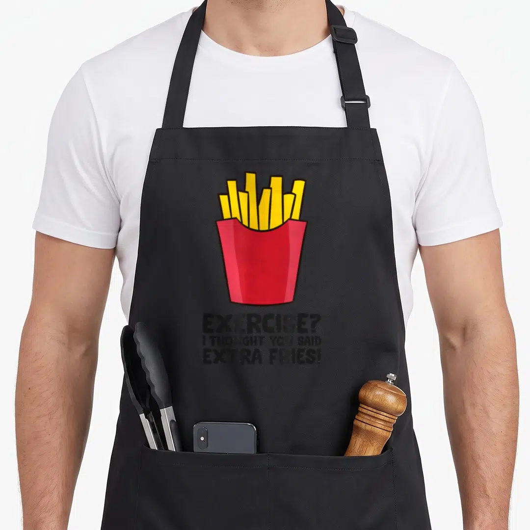 Exercise thought an extra apron - Cartoon red fry container with yellow sticks and stacked text reading EXERCISE? I — shown on a black cotton canvas apron against a white background