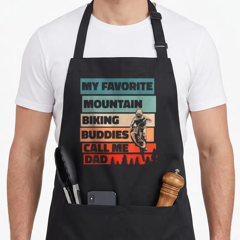 Mountain buddy aprons - Stacked text reading My Favorite Mountain Biking Buddies Call Me Dad with biker silhouette — shown on a black cotton canvas apron against a white background