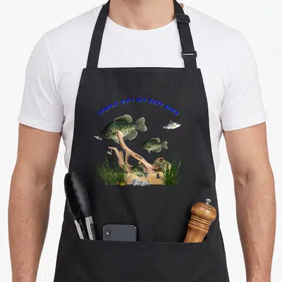 Crappie outdoor apron - Four crappie fish swimming near driftwood and grass under arched blue text — shown on a black cotton canvas apron against a white background