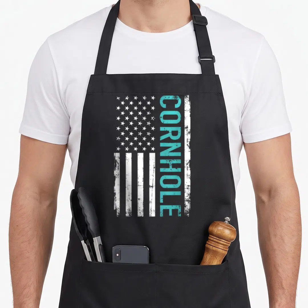 Cornhole corn on the cob apron - Vertical distressed USA flag with teal CORNHOLE text replacing a stripe and white stars — shown on a black cotton canvas apron against a white background