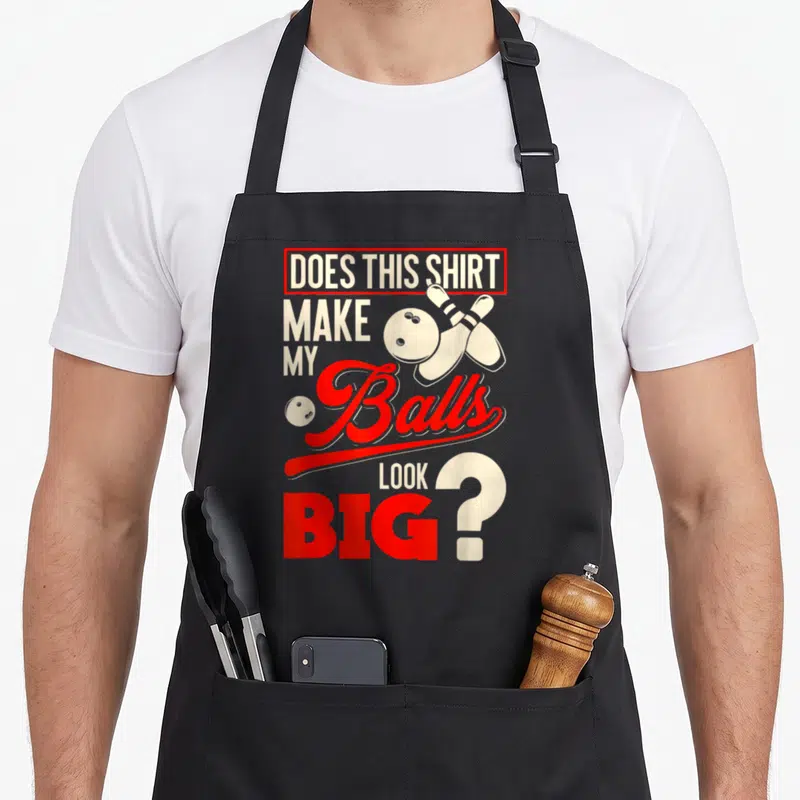 Ball bowling apron - Red and white text DOES THIS SHIRT MAKE MY Balls LOOK BIG with crossed pins and bowling balls — shown on a black cotton canvas apron against a white background