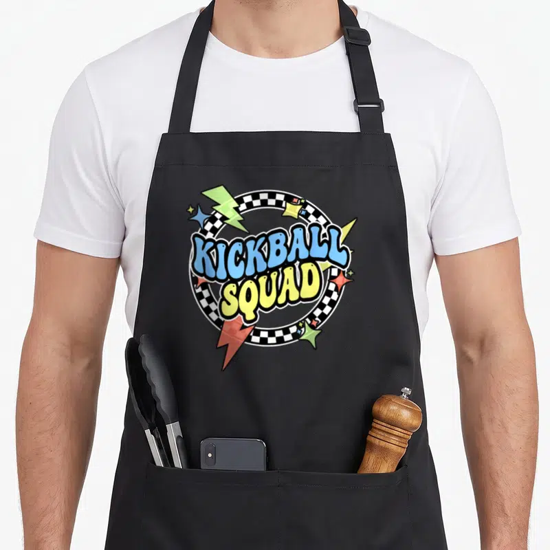 Squad ready kick apron - KICKBALL SQUAD text in blue and yellow inside a checkered circle with lightning bolts and stars — shown on a black cotton canvas apron against a white background