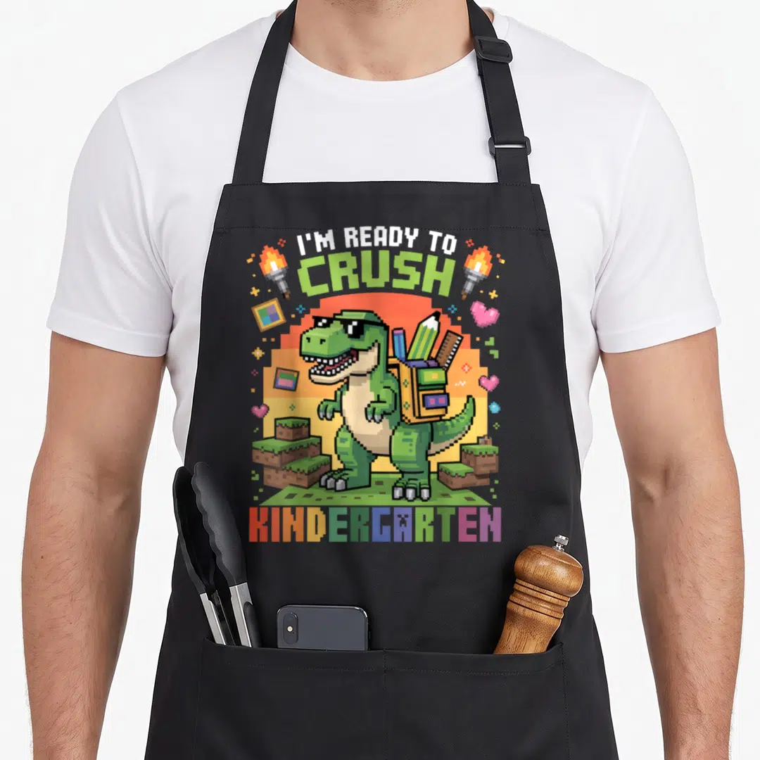 School kindergarten dinosaur apron - Pixelated green T-Rex with backpack and I'm Ready To Crush Kindergarten text — shown on a black cotton canvas apron against a white background