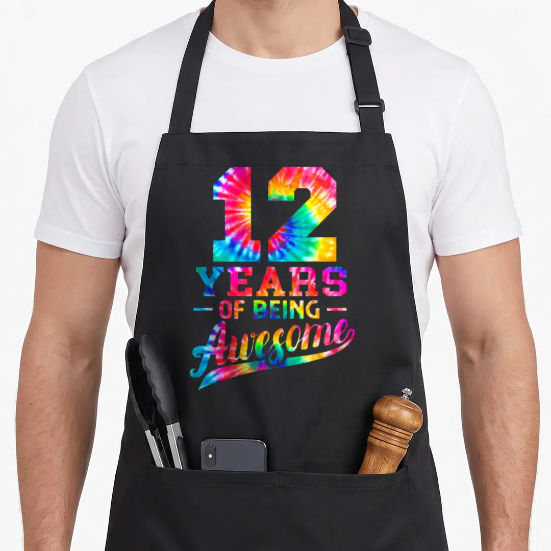 12th tie apron - Tie-dye text reading 12 Years of Being Awesome with pink blue yellow green colors and swoosh — shown on a black cotton canvas apron against a white background