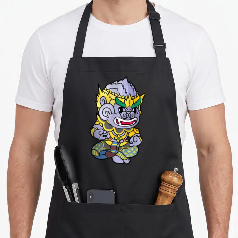 Cambodian king apron - Cartoon Hanuman Monkey King seated in yellow armor with purple skin and green crown accents — shown on a black cotton canvas apron against a white background