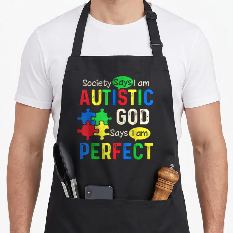 Society autism awareness apron - Stacked text reading AUTISTIC and PERFECT with four colorful puzzle pieces in red — shown on a black cotton canvas apron against a white background