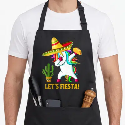 Cinco unicorn apron - Cartoon white unicorn dabbing in sombrero holding taco next to cactus with LET'S FIESTA text — shown on a black cotton canvas apron against a white background