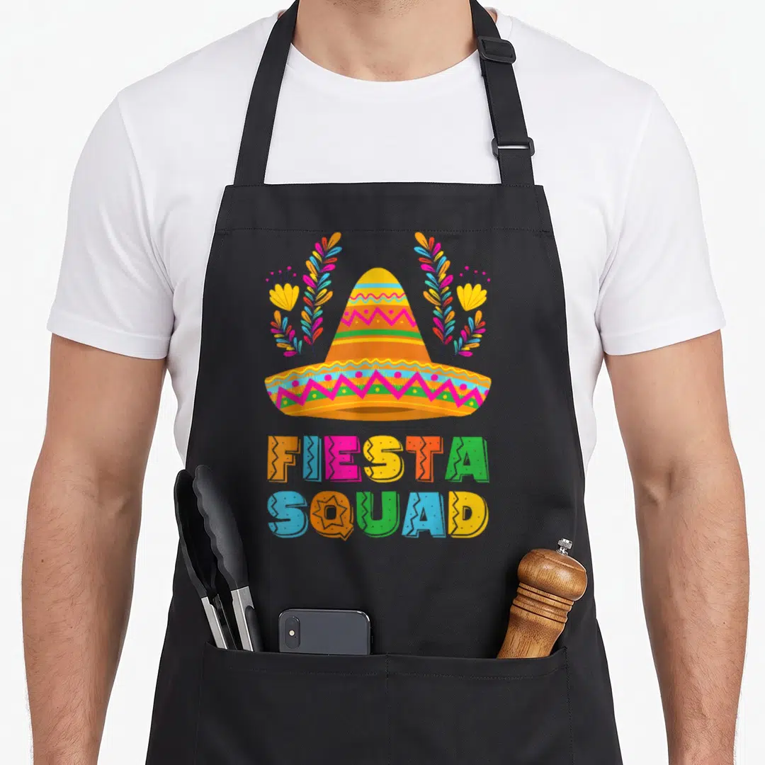 Cinco family aprons - Colorful sombrero with FIESTA SQUAD text and symmetrical floral decorations in cartoon style — shown on a black cotton canvas apron against a white background