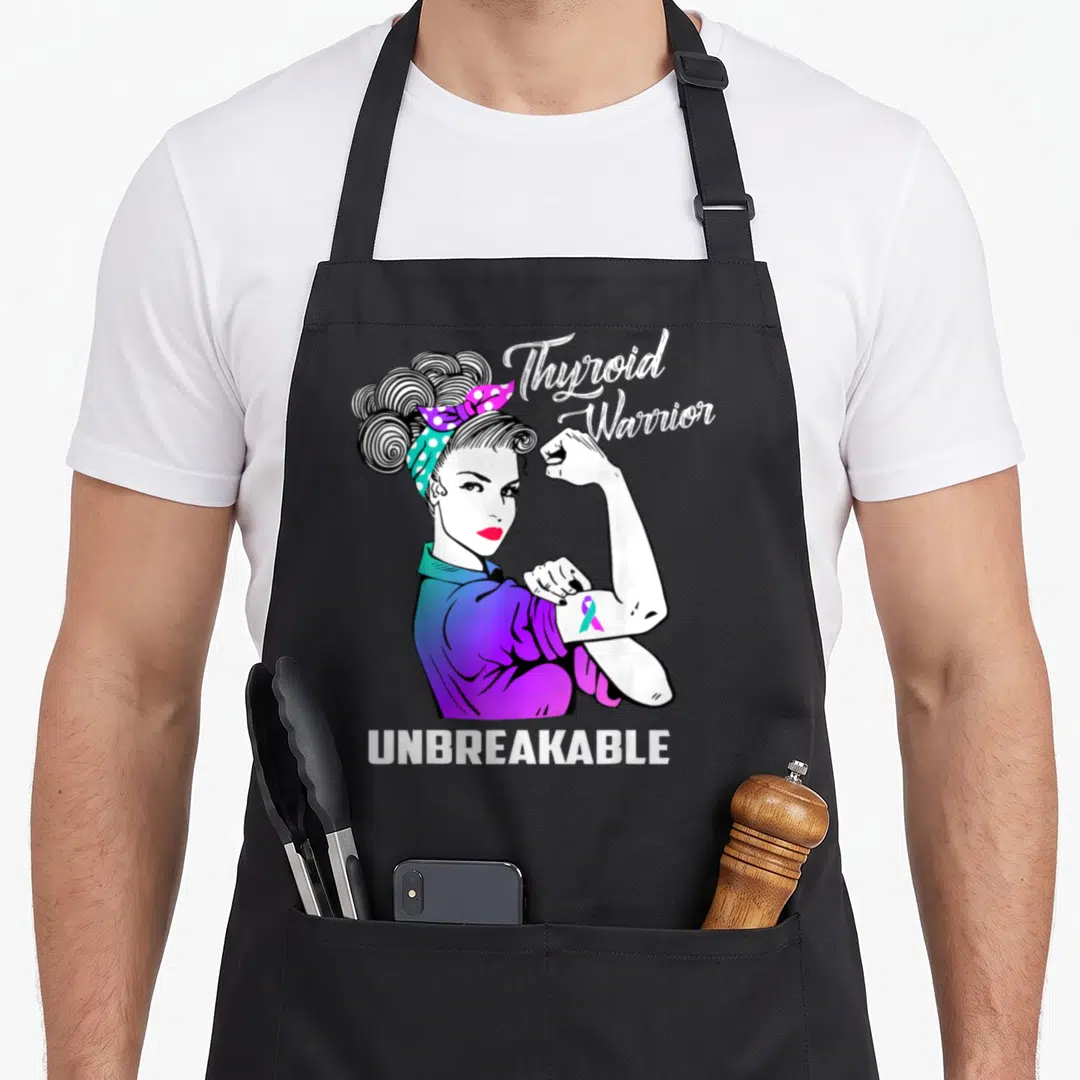 Warrior thyroid apron - Woman flexing arm with Thyroid Warrior text and purple teal ribbon in cartoon style — shown on a black cotton canvas apron against a white background