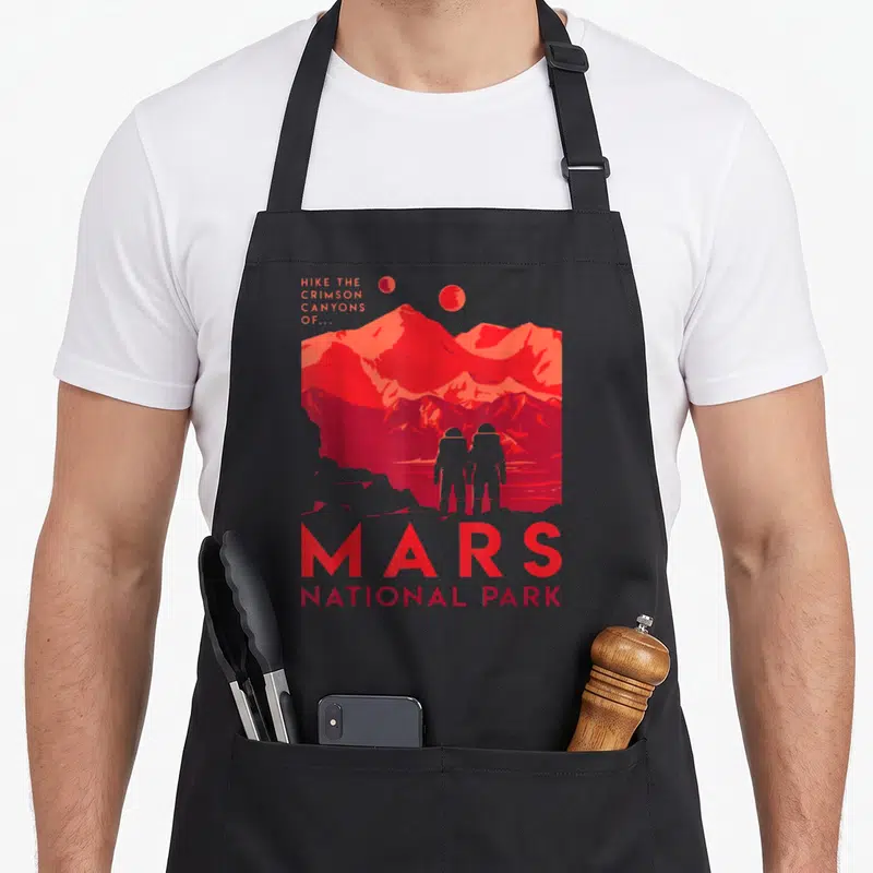National space planets apron - Red minimalist Mars landscape with two astronauts, two moons, and stacked text reading — shown on a black cotton canvas apron against a white background