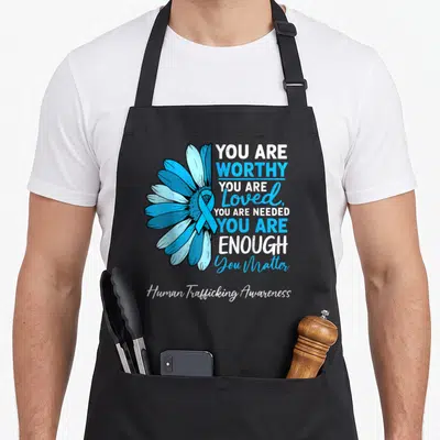 Human sunflower apron - Blue daisy with ribbon and text You Are Worthy Enough Human Trafficking Awareness — shown on a black cotton canvas apron against a white background