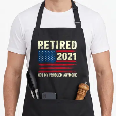 Vintage problem retirement apron - Distressed USA flag with Retired 2021 and Not My Problem Anymore text in beige — shown on a black cotton canvas apron against a white background