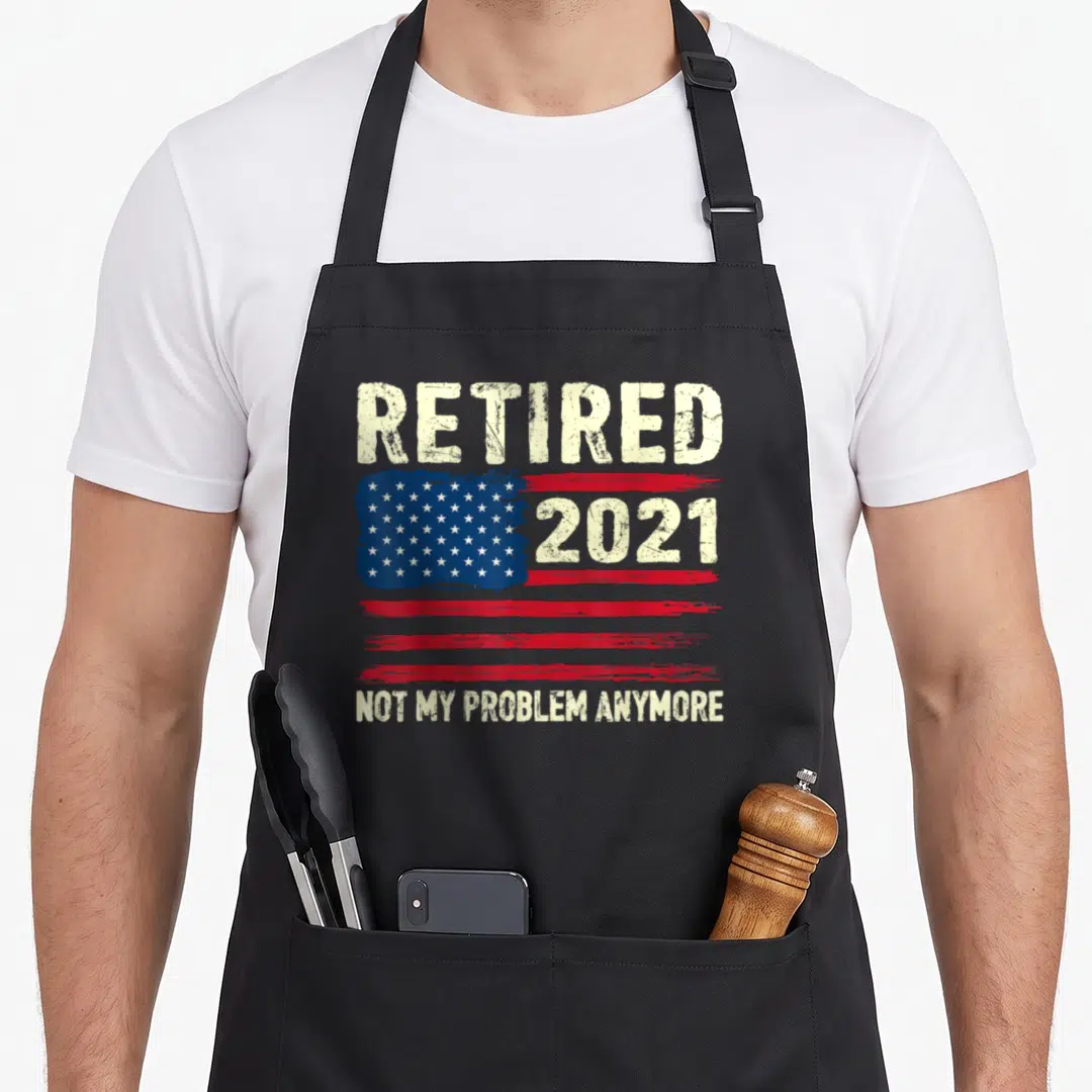 Vintage problem retirement apron - Distressed USA flag with Retired 2021 and Not My Problem Anymore text in beige — shown on a black cotton canvas apron against a white background