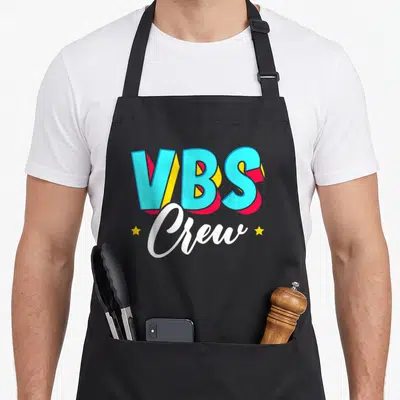 Crew paint splatter apron - VBS Crew 3D text in blue red yellow with two stars and script lettering — shown on a black cotton canvas apron against a white background