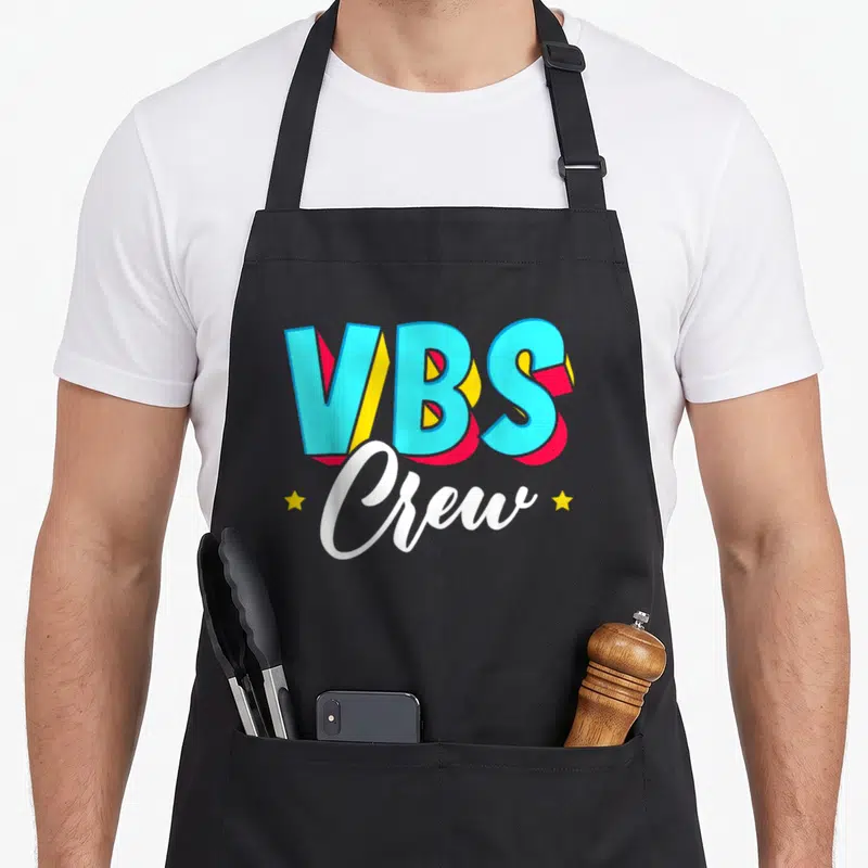 Crew paint splatter apron - VBS Crew 3D text in blue red yellow with two stars and script lettering — shown on a black cotton canvas apron against a white background