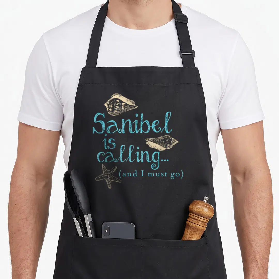 Sanibel florida apron - Blue script text with beige seashells and starfish line art on dark background — shown on a black cotton canvas apron against a white background