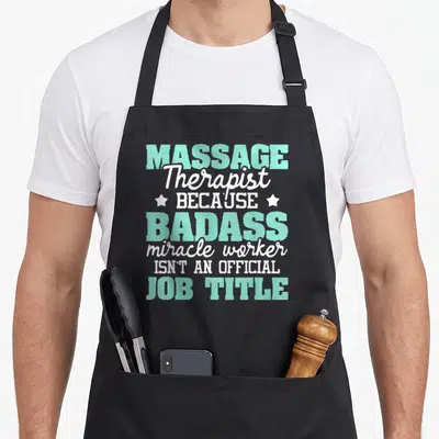 Massager massage therapy apron - Mint and white text reading MASSAGE Therapist BADASS miracle worker with two stars — shown on a black cotton canvas apron against a white background