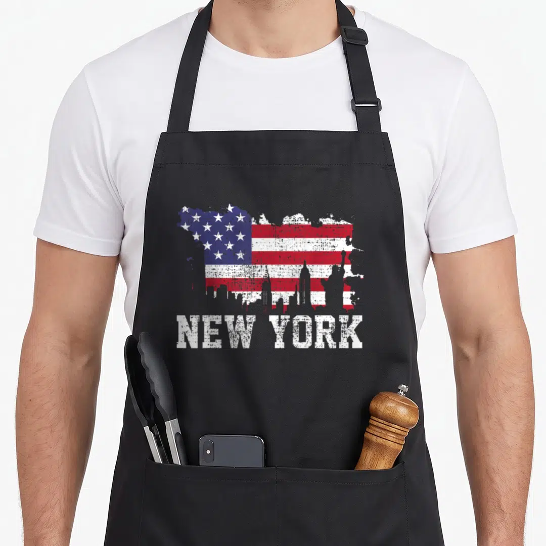 Flag new york apron - Distressed USA flag paint splatter with white skyline silhouette and NEW YORK text below — shown on a black cotton canvas apron against a white background