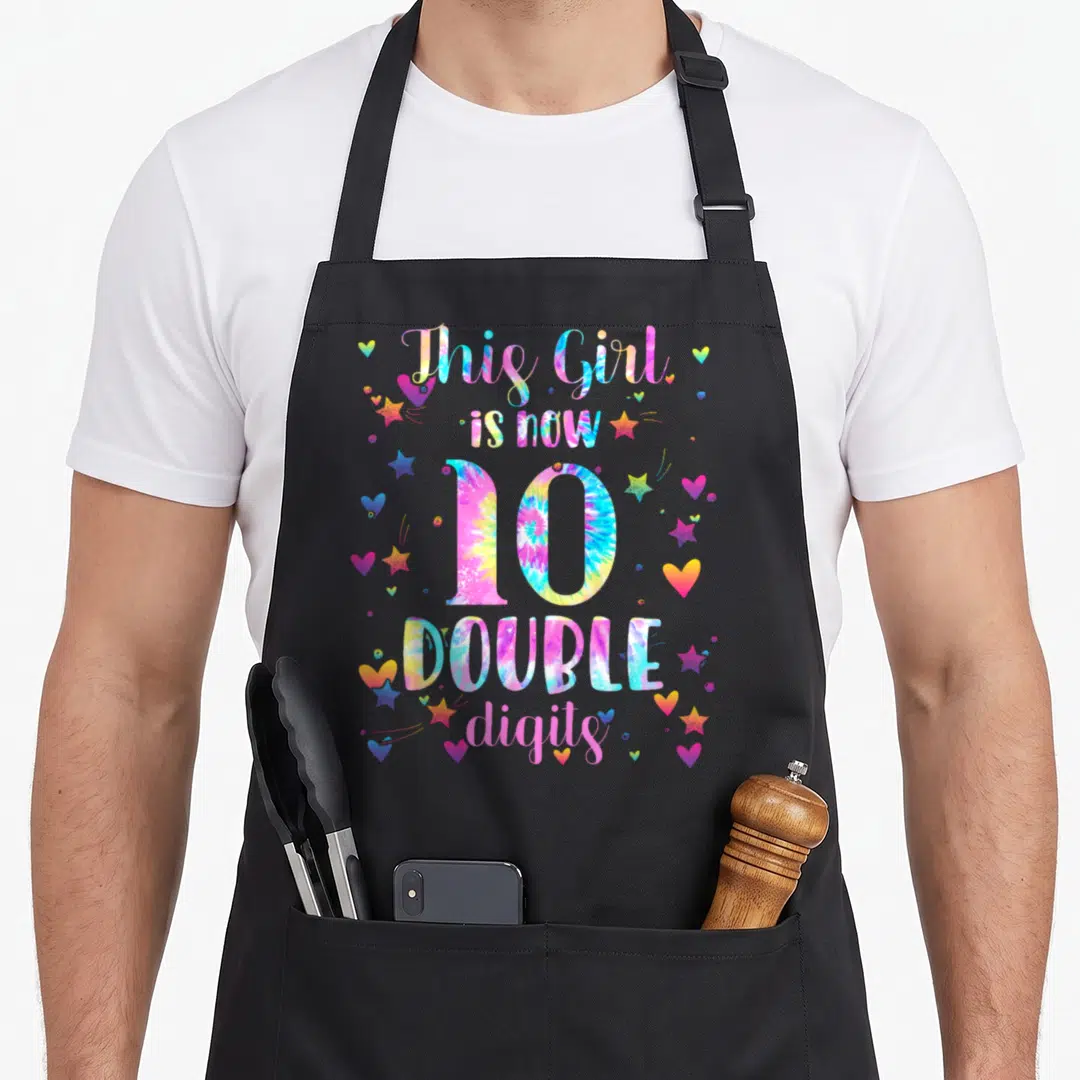10th tie-dye apron - Tie-dye text This Girl is now 10 Double digits with pink blue yellow purple hearts and stars — shown on a black cotton canvas apron against a white background