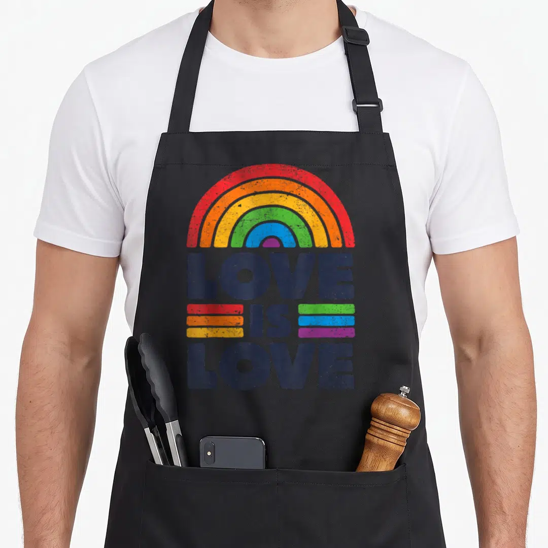 Ally rainbow flag gay pride apron - LOVE IS LOVE text under rainbow arch with colored stripes in distressed print — shown on a black cotton canvas apron against a white background