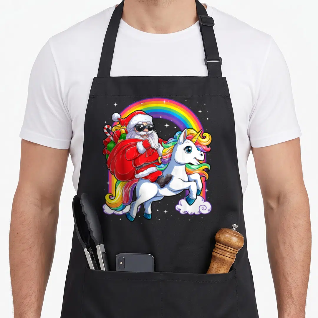 Riding christmas santa apron - Cartoon Santa in sunglasses riding a rainbow-maned unicorn under an arch with clouds — shown on a black cotton canvas apron against a white background