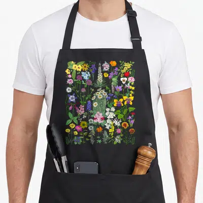 Flower wildflower floral apron - Cartoon illustration of diverse wildflowers and a central cactus in green, yellow — shown on a black cotton canvas apron against a white background