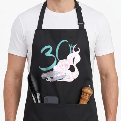 Ariel birthday apron - Pink mermaid illustration overlapping a large blue 30 with birthday text below — shown on a black cotton canvas apron against a white background