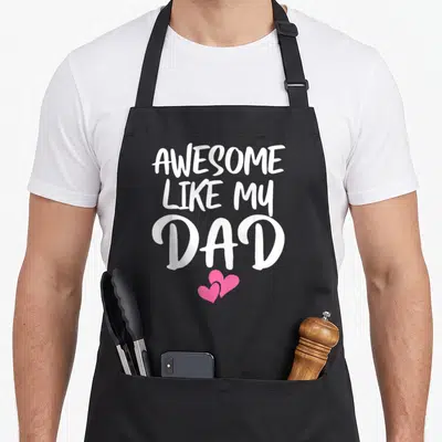 Son mom daughter aprons - White stacked text AWESOME LIKE MY DAD with two pink hearts on black fabric — shown on a black cotton canvas apron against a white background
