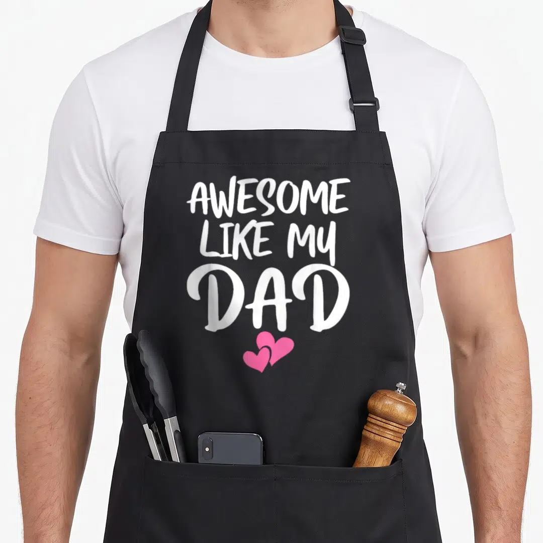 Son mom daughter aprons - White stacked text AWESOME LIKE MY DAD with two pink hearts on black fabric — shown on a black cotton canvas apron against a white background