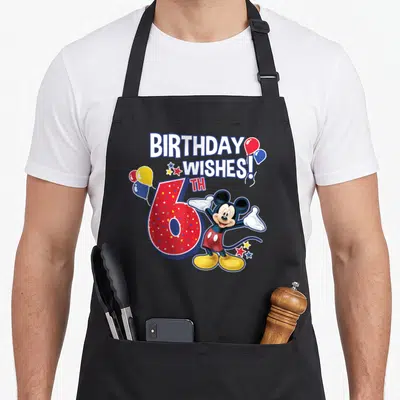 6th friends apron - Mickey Mouse next to red polka dot number 6 and BIRTHDAY WISHES text with balloons — shown on a black cotton canvas apron against a white background