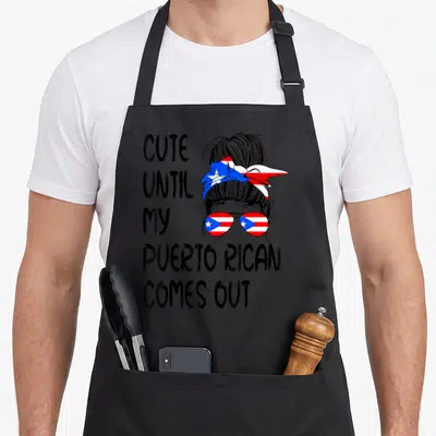 Rican puerto boy apron - Stacked text next to woman with flag sunglasses and bun in line art — shown on a black cotton canvas apron against a white background