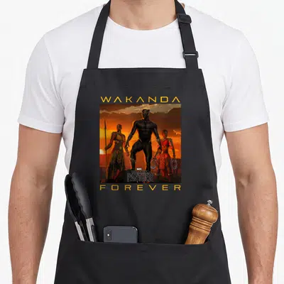 Forever wakanda apron - Three characters stand in a row under WAKANDA and FOREVER text against an orange sunset — shown on a black cotton canvas apron against a white background
