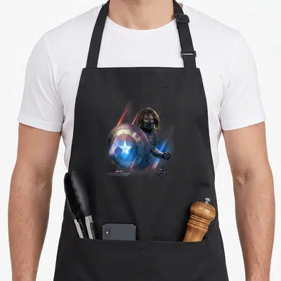 Shield winter apron - Captain America holding shield with motion blur lines and Marvel Studios text — shown on a black cotton canvas apron against a white background