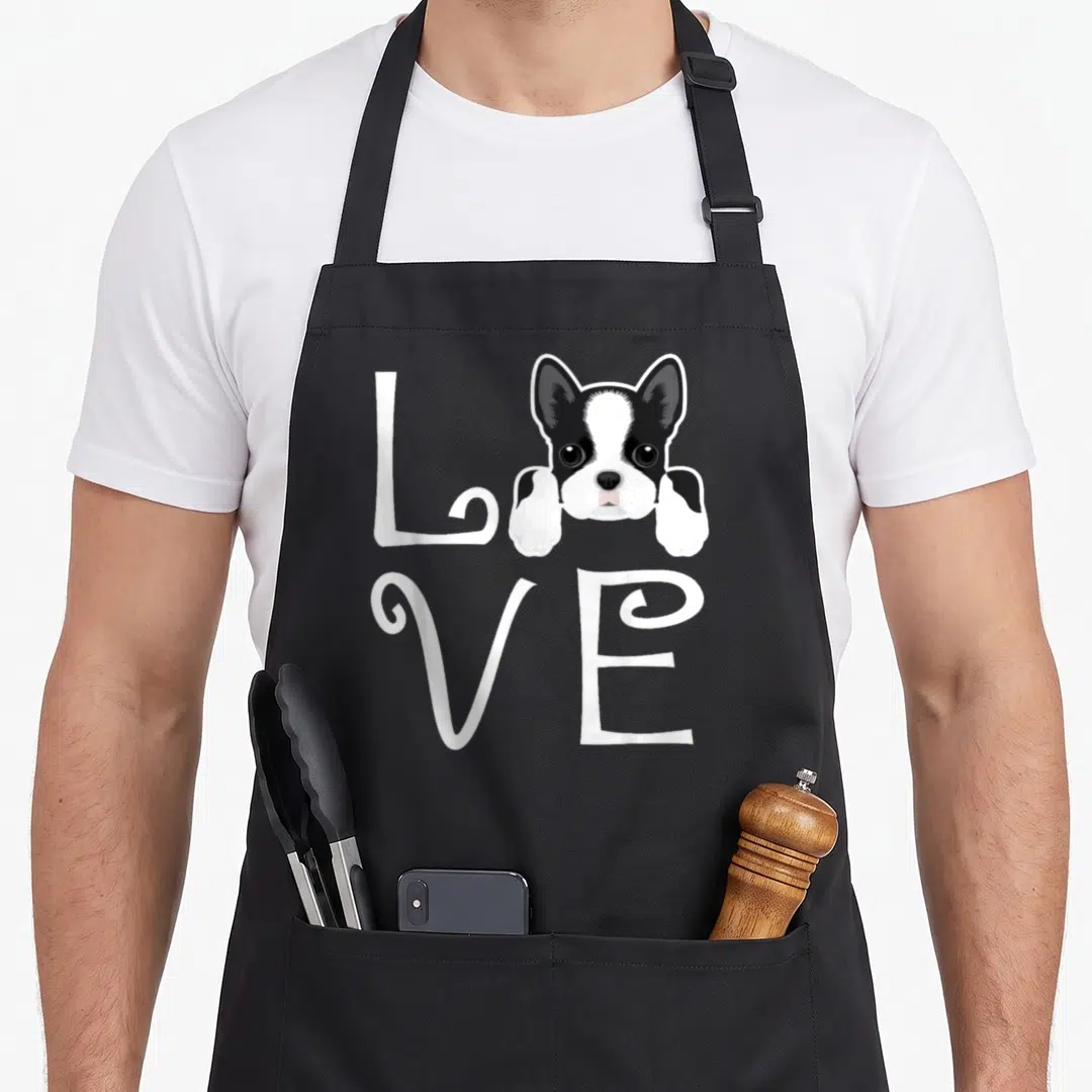 Terrier owner dog apron - Cartoon Boston Terrier head and paws replacing the O in white LOVE script — shown on a black cotton canvas apron against a white background