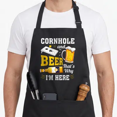 Cornhole beer apron - Stacked text CORNHOLE BEER with board, mug, bottle in white yellow orange distressed style — shown on a black cotton canvas apron against a white background