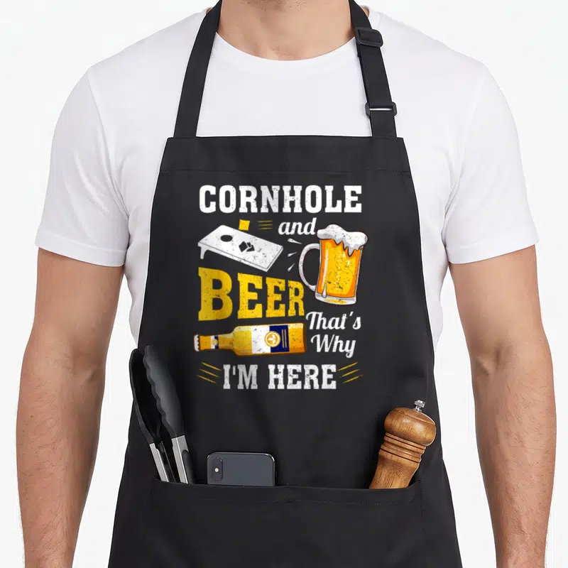 Cornhole beer apron - Stacked text CORNHOLE BEER with board, mug, bottle in white yellow orange distressed style — shown on a black cotton canvas apron against a white background
