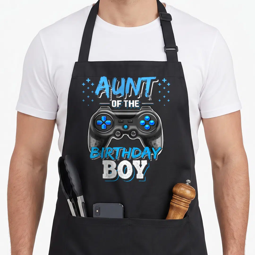Aunt birthday video game apron - Cartoon black controller with blue plus signs and stacked Aunt of the Birthday Boy text — shown on a black cotton canvas apron against a white background