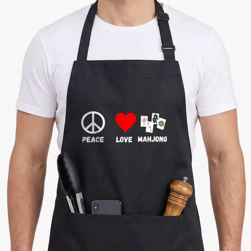 Peace mahjong apron - Three symbols: white peace sign, red heart, and mahjong tiles with text below each in white — shown on a black cotton canvas apron against a white background