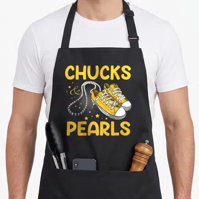 Vintage chuck pearls apron - Yellow sneakers and pearl necklace flanked by CHUCKS and PEARLS text with stars — shown on a black cotton canvas apron against a white background