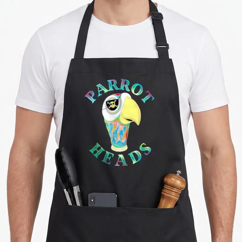 Parrot creative apron - Cartoon parrot head with skull eyepatch and arched multicolor text — shown on a black cotton canvas apron against a white background