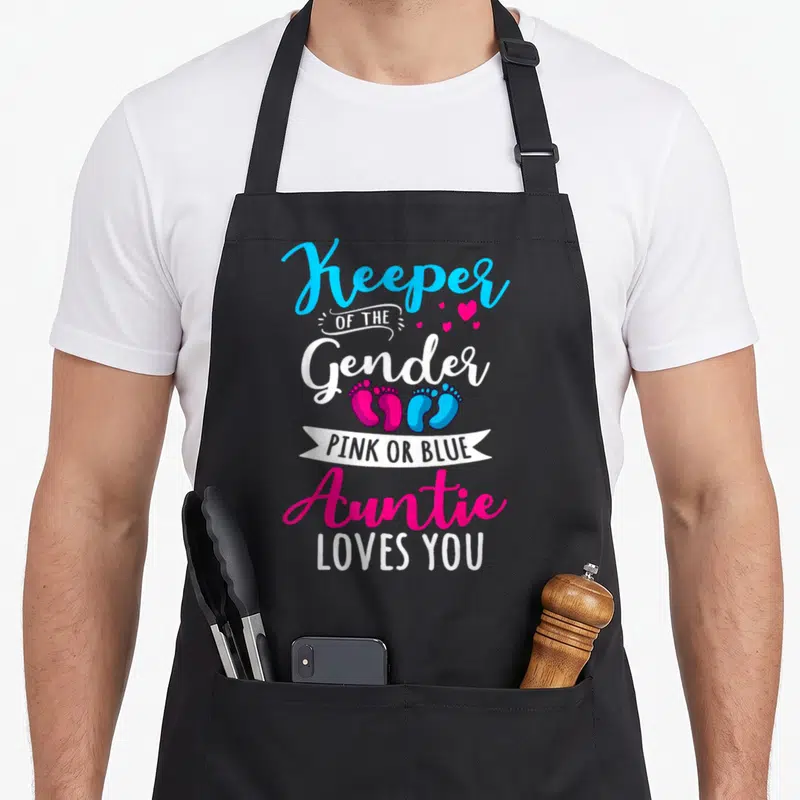 Keeper aunt apron - Stacked text Keeper of Gender with pink and blue footprints and white ribbon banner — shown on a black cotton canvas apron against a white background