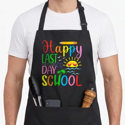 Student graduation teacher apron - Colorful Happy Last Day of School text with sun sunglasses pencil and palm tree — shown on a black cotton canvas apron against a white background