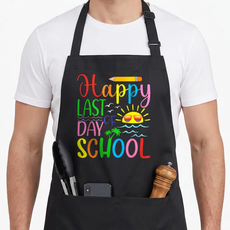 Student graduation teacher apron - Colorful Happy Last Day of School text with sun sunglasses pencil and palm tree — shown on a black cotton canvas apron against a white background