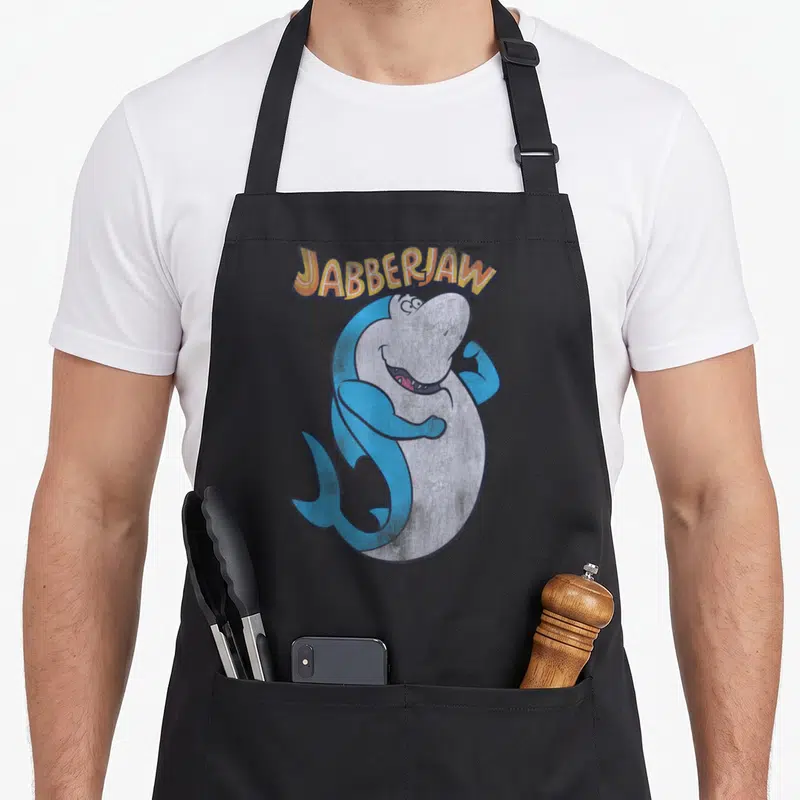Jabberjaw distressed apron - Arched JABBERJAW text above a flexing blue cartoon shark with distressed texture — shown on a black cotton canvas apron against a white background