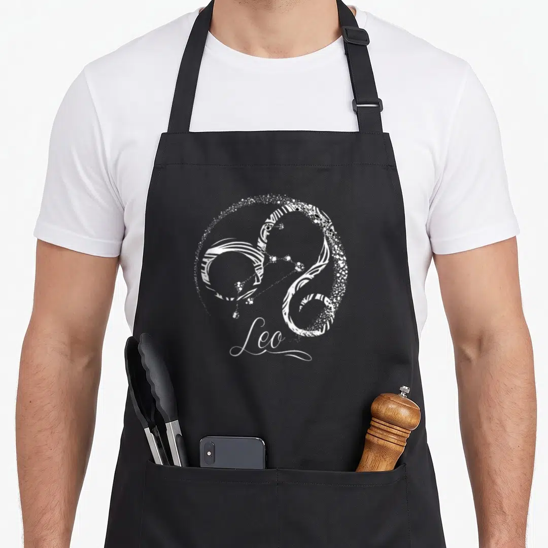 July august birthday apron - White stylized Leo zodiac symbol made of lines and dots with script text below — shown on a black cotton canvas apron against a white background