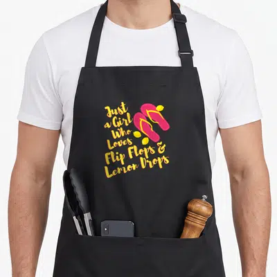 Flip for love and lemons apron - Stacked yellow text next to two pink flip flops and three yellow lemon drops — shown on a black cotton canvas apron against a white background