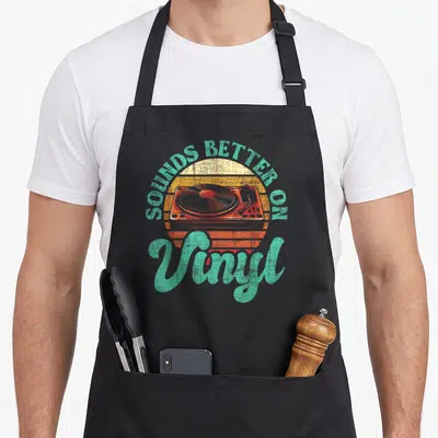 Collector vinyl apron - Retro turntable and sounds better on vinyl text in teal and orange — shown on a black cotton canvas apron against a white background