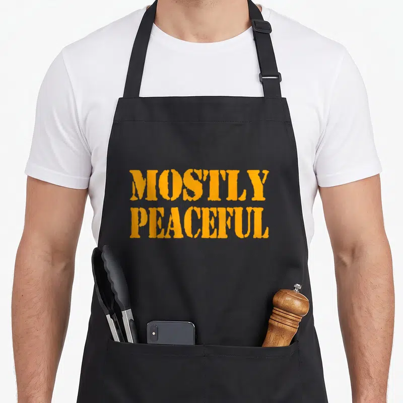 Mostly peaceful apron - Orange stacked text MOSTLY PEACEFUL on black fabric — shown on a black cotton canvas apron against a white background