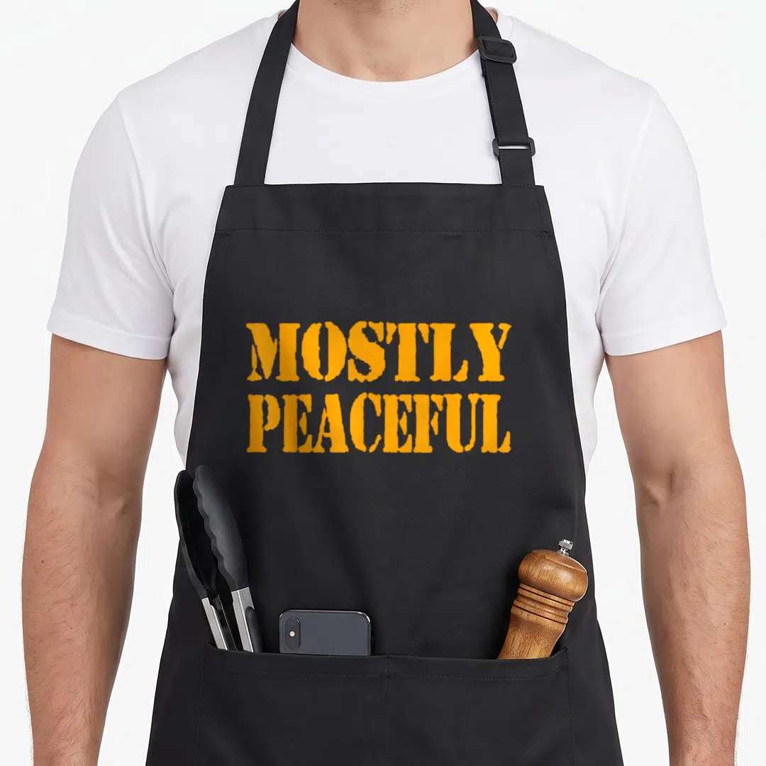 Mostly peaceful apron - Orange stacked text MOSTLY PEACEFUL on black fabric — shown on a black cotton canvas apron against a white background